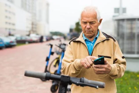 Old man using smartphone to activate e-scooter Foto stock