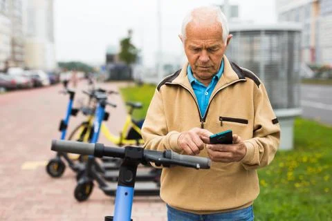 Old man using smartphone to activate e-scooter Stock Photos