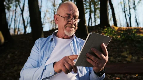 Old man is using tablet computer in the park. Senior man with a beard and Stock Footage 97794324