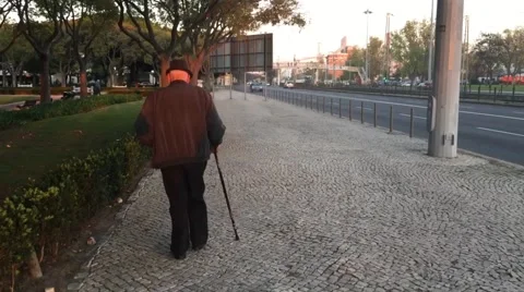 Old man walking alone with walking stick on a pavement near freeway Stock Footage