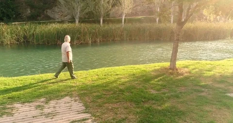 Old man walking along the river bank at sunset Stock Footage 124382306