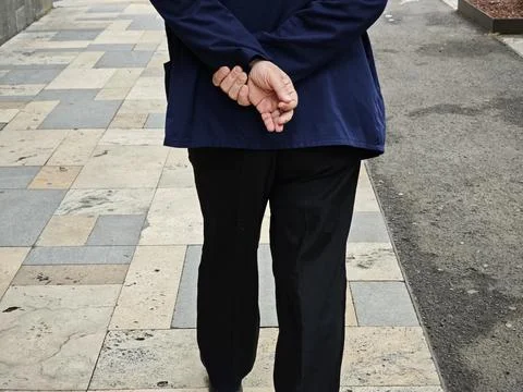 Old man walking away on a patterned sidewalk with his hands behind his back Stock-Fotos