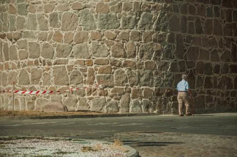Old man walking in front of the thick city wall of Avila Stock Photos