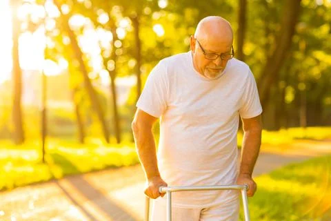 Old man is walking with walker outdoor at sunset. Rehabilitation concept. Stock Photos