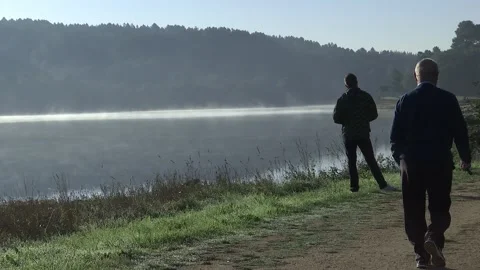 OLD MAN WALKING WHILE ANOTHER MAN WATCHES THE FOG OVER THE LAKE Stock Footage 97305923