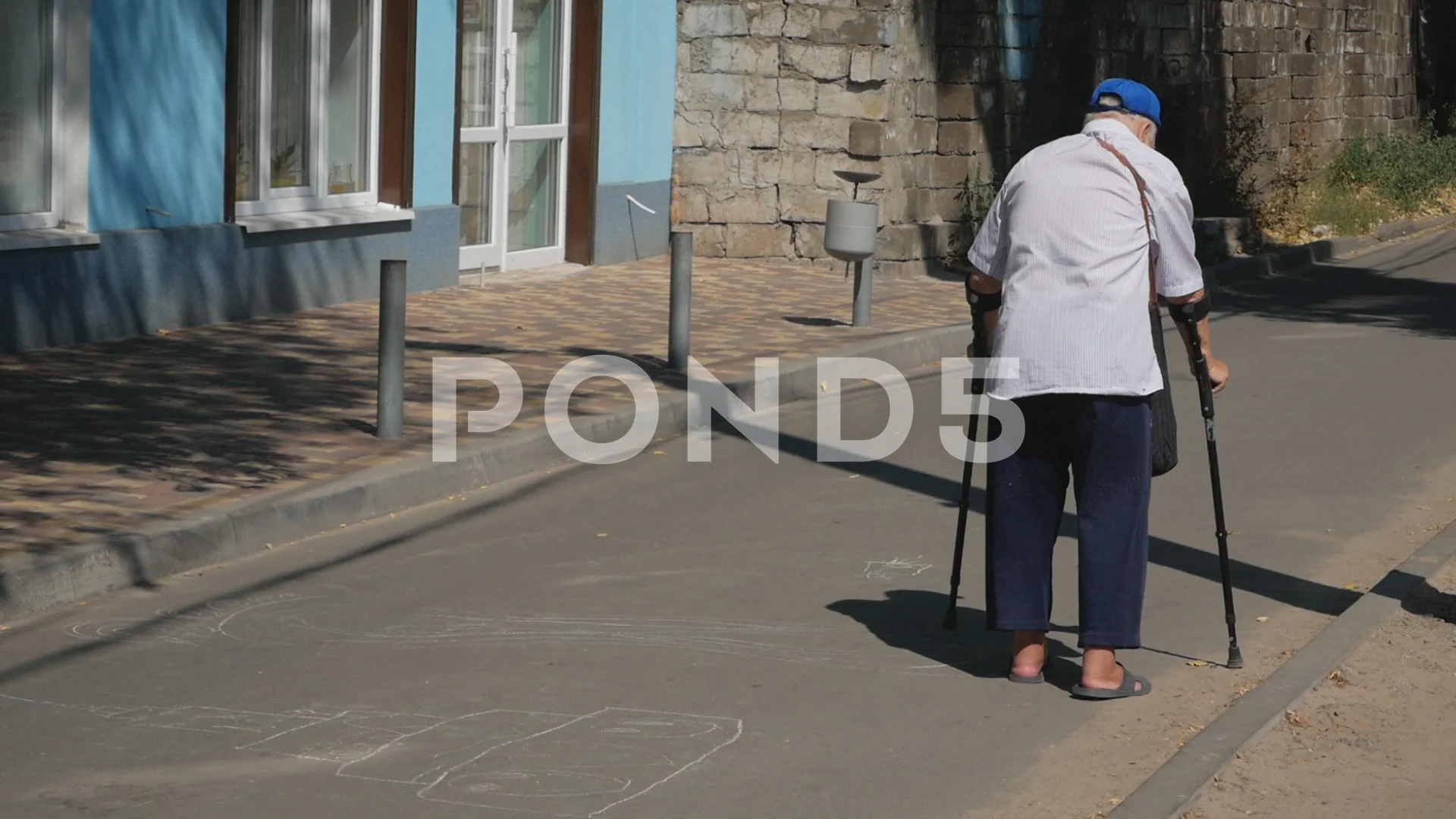 Old man walks hard along the road with crutches