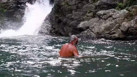 Old man washes in a waterfall. Video stock 122964658