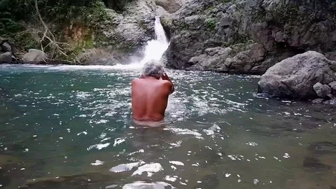 Old man washes in a waterfall. Video stock 122965055