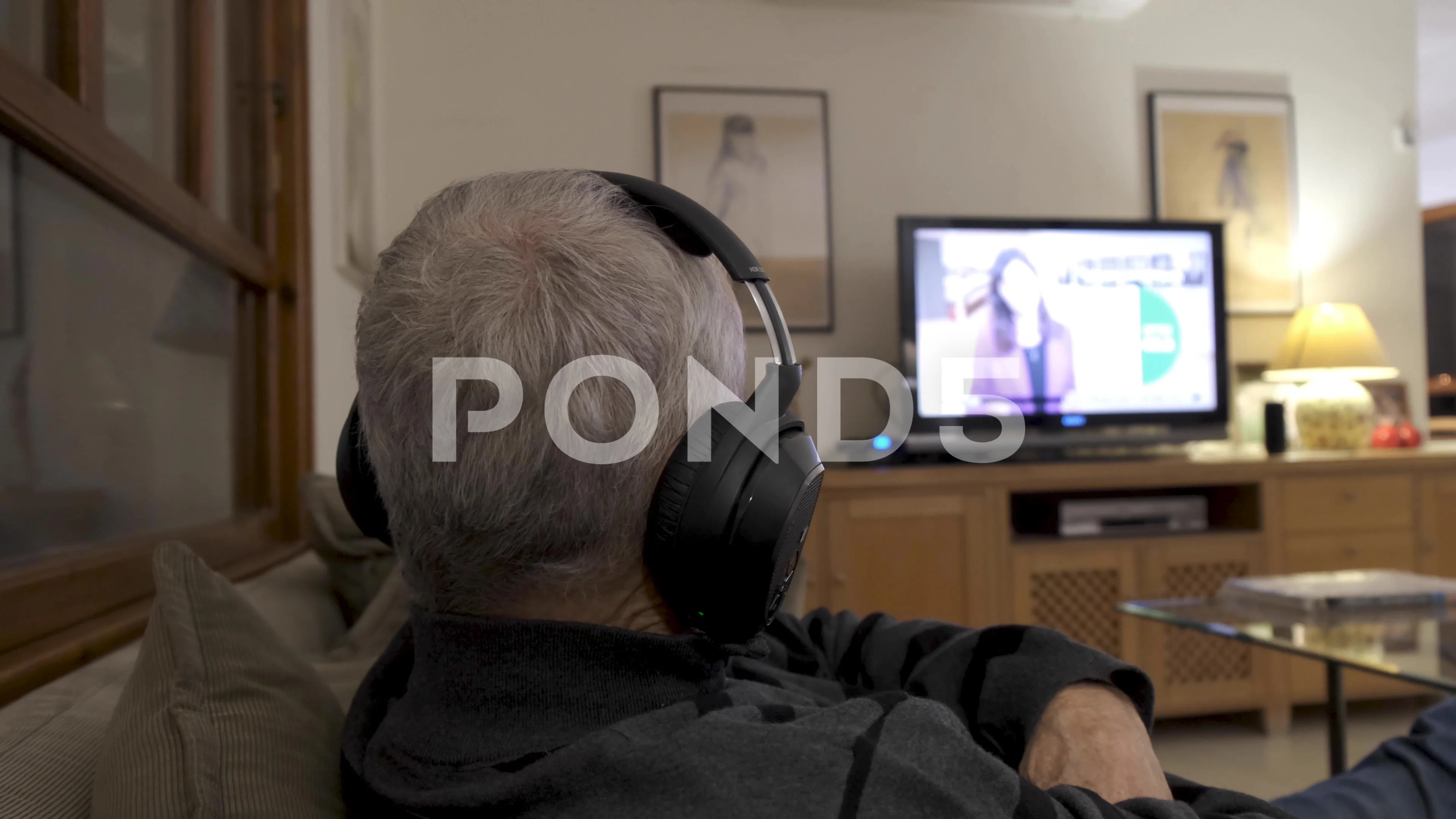 Old man watching tv with headphones. Man wears a hearing aid