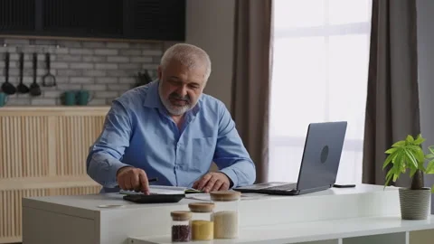 Old man is working at home, making calculations and looking info in laptop Stock Footage 153510844
