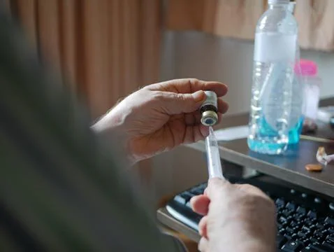 An old man's hands carefully pulling the medicine into the syringe by himself Stock Photos