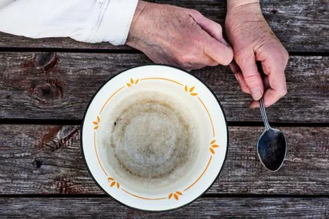 Old man's hands hold an empty old bowl and spoon Stock Photos