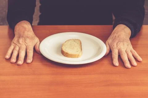 Old man's hands on table with one slice of bread in middle Stock Photos