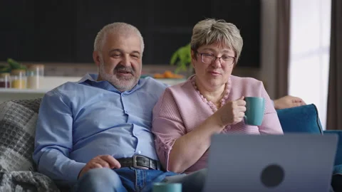 Old married pair is viewing video or movie on laptop, sitting together in living Stock Footage 153512875