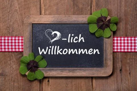 Old menu board with welcome message in german - clovers and ribbon on wooden Foto stock