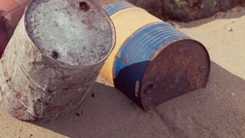 Old metal barrels sit on sandy shore by the ocean in bright sunlight Stock Footage 343936599
