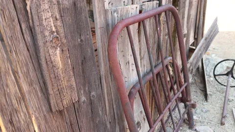 An old metal bed frame leaning against a ghost town building with shallow DOF Stock Footage 201193279