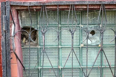 Old metal grate over broken glass brick window in weathered red brick wall Stock Photos