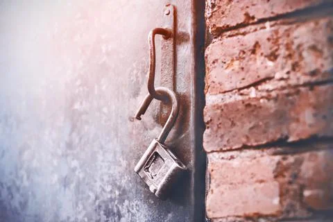 An old metal open lock hangs on the handle of an iron door, standing in a bri Stock Photos