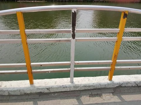 Old metal railing with yellow posts overlooking a green water surface structure Stock Photos