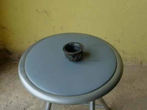 Old metal threaded coupling lying on round stool seat against yellow wall bac Stock Photos