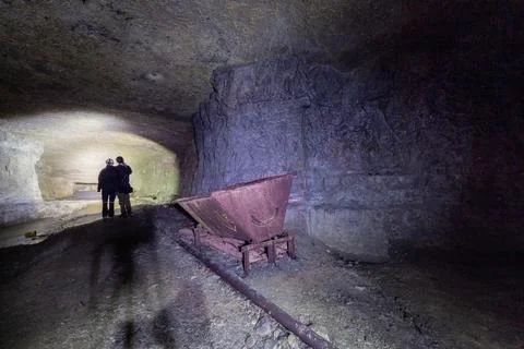 Old mine, deep underground, with an old lorry on rails. Siloette of a couple. Stock Photos