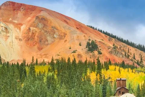 An old mining headframe stands surrounded by autumn foliage below Red Mount.. Stock Photos