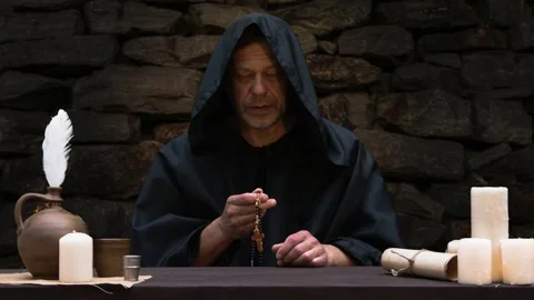 Old monk in cassock holding Catholic rosary in his hand and reciting a prayer ag Stock Footage 274455697