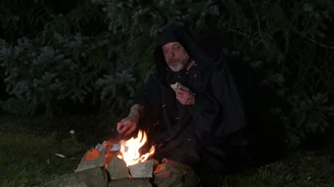 An old monk eating his supper at night in the woods by the fire. Stock Footage 303783311