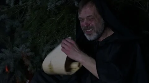 An old monk in a robe studies a manuscript by the light of a campfire flame in t Video stock 303783129