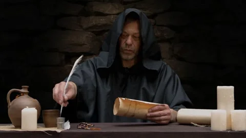 An old monk writes with a quill pen in a scroll or parchment, sitting at a table Video stock 274455845