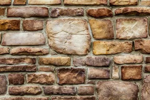 Old odd shaped tan and brown thick cut stone block wall Stock Photos
