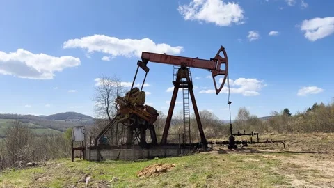 Old Oil Pump Jack Operating in Rural Field.Working oil well pump on muddy Stock Footage 314940266
