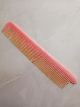 Old Orange Comb with Broken Teeth Lying on Ceramic Floor 스톡 사진