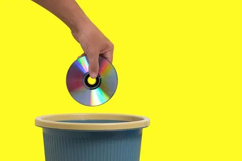 Old, outdated CD in your hand is thrown into trash.Yellow background. Stock Photos