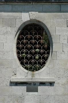 An Old Oval Stone Window with an Ornate Wrought Iron Decorative Grille Stock Photos