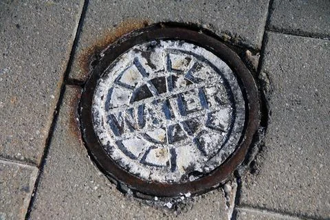An old oxidized water manhole on a public walkaway Stock Photos