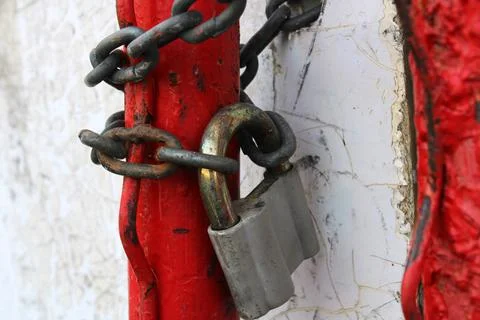 An old padlock on a rusty chain wrapped around red pipes.. Stock Photos