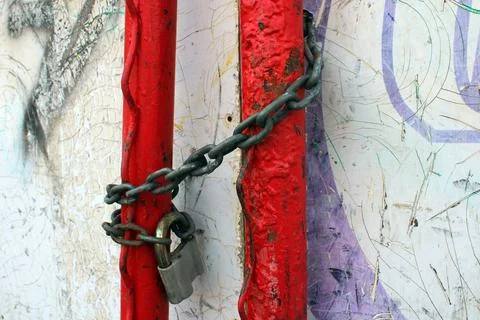 An old padlock on a rusty chain wrapped around red pipes Stock Photos