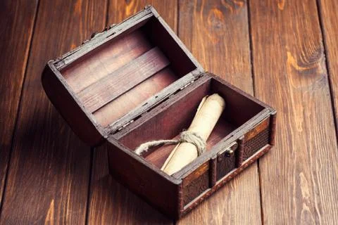 Old paper roll inside treasure chest on wooden background Stock Photos