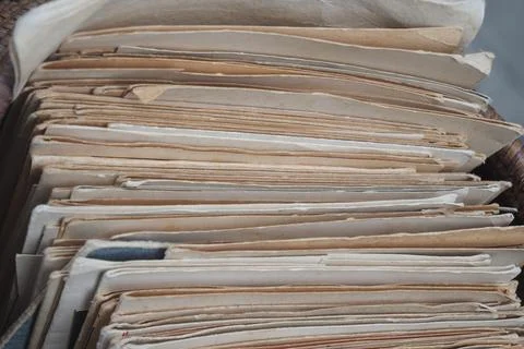 Old papers stacked in a box showing signs of age Stock Photos
