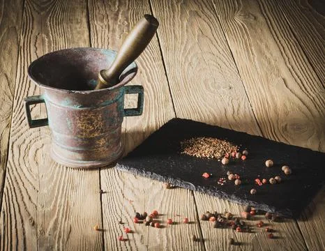 An old patina-covered bronze pepper mortar stands on a wooden table Stock Photos