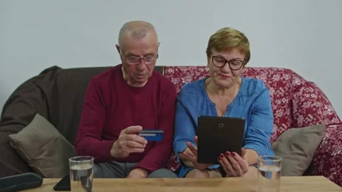 Old people are sitting on the sofa using a credit card and digital tablet. Stock Footage 157937608