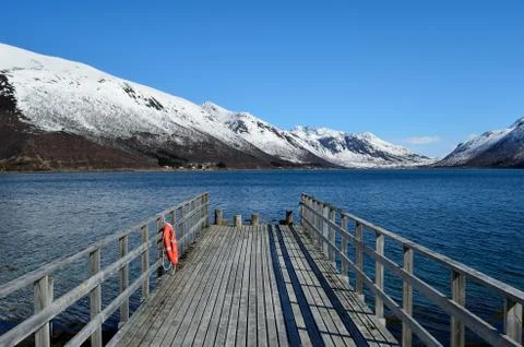 Old pier going into the deep blue fjord with snowy mountain backdrop in nor.. 写真素材
