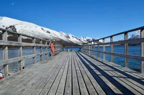 Old pier going into the deep blue fjord with snowy mountain backdrop in nor.. Stock Photos