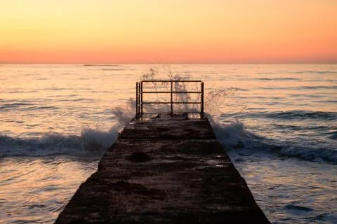 Old pier with waves at sunset Stock Photos