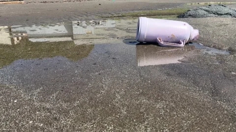 Old pink plastic flask trash in a puddle on a beach Stock Footage 272578497