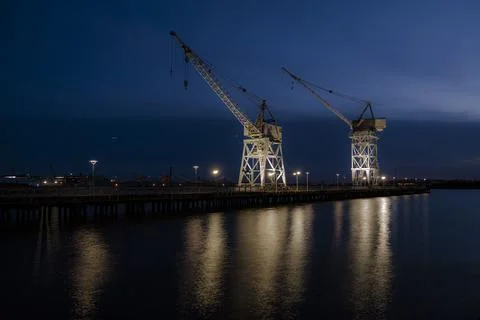 Old port cranes at night with reflection in the water Stock Photos