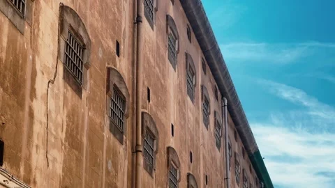 Old prison building with barred windows against blue sky, historic architecture Stock Footage 334713742