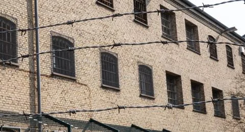 Old prison building with bars on the windows and barbed wire fence Stock Photos